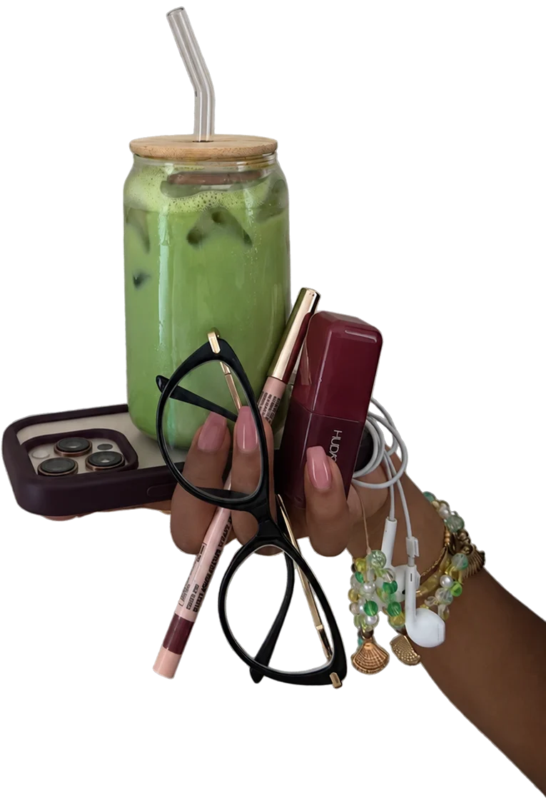 Une main tient un matcha glacé, un téléphone, des lunettes, du maquillage et des écouteurs